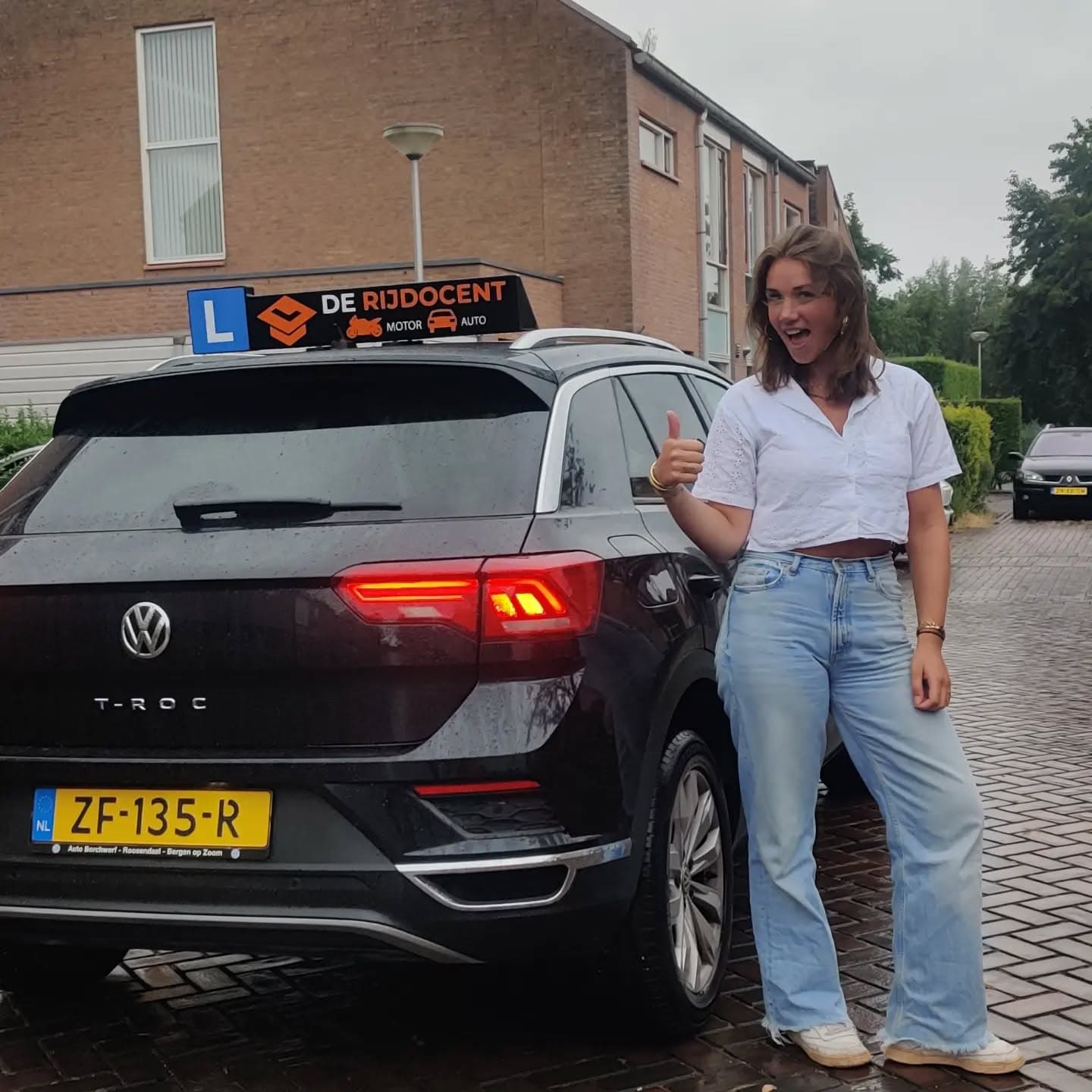 Geslaagde leerling met duim omhoog bij de lesauto van De Rijdocent